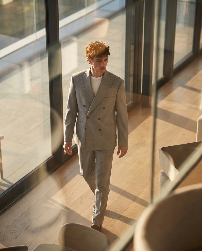 AI-generated background, same suit in a sunlit glass corridor with wood flooring